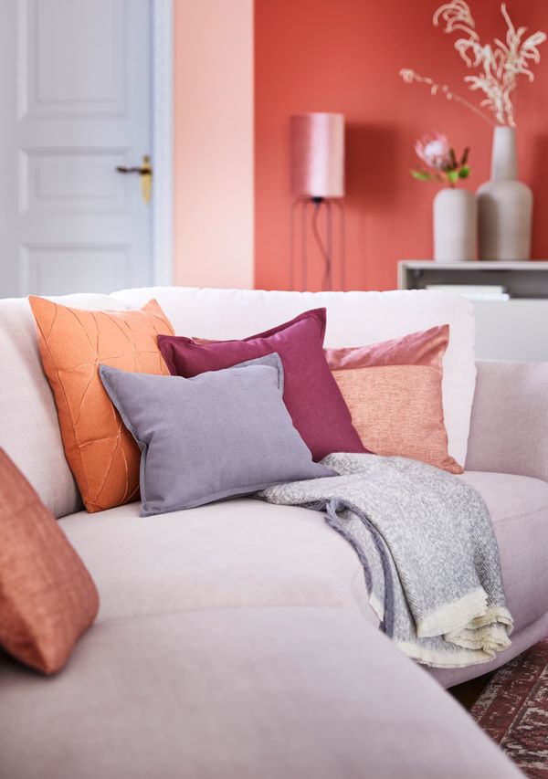 Wohnzimmer mit rosa Rundsofa und bunten Kissen SCHÖNER WOHNEN-Heimtextilien